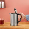 A hand holding a kettle over a wooden surface with a mug of tea. Voir les images du produit