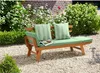 A wooden garden bench with green cushions and pillows is placed on a gravel path in a garden setting, surrounded by lush greenery and a brick wall. Produktbild-Vorschau