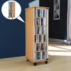 A tall, narrow wooden CD storage cabinet with glass doors, filled with CDs, is shown in a room with a dark blue wall and light wooden floor. Produktbild-Vorschau