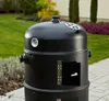 A black smoker grill is shown in a backyard setting with green grass and plants in the background. Náhled obrázku produktu