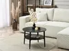 A round coffee table with a marble top and two shelves is placed in a living room setting next to a white sofa. Produktbild-Vorschau