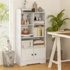 A white bookshelf filled with books and decorative items, placed next to a window and a desk with a plant. Produktbild-Vorschau