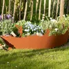A decorative metal garden border with a fairy motif, separating a flower bed from a lawn, with a wooden fence in the background. Produktbild-Vorschau