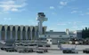 An airport scene with a control tower and terminal building, with various airport vehicles and equipment in the foreground. Anteprima dell’immagine prodotto