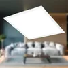 A white LED panel light is shown in the foreground, with a blurred living room scene in the background. Podgląd zdjęcia produktu