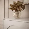 A close-up shot of dried flowers in a glass vase on top of a white dresser. Produktbild-Vorschau