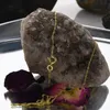 A gold necklace is displayed on a large crystal formation, with rose petals in the foreground. Produktbild-Vorschau