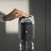 A hand is shown pressing the top of a black water carbonator device, which is attached to a glass bottle. Produktbild-Vorschau