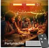 People enjoying a meal outdoors at night, with string lights and a patio heater. Produktbild-Vorschau