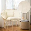 A beige macrame hanging chair with cream cushions is placed near a window, with a woven basket next to it. Podgląd zdjęcia produktu