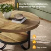 A round coffee table with a rustic wood finish and black metal legs, shown in a living room setting with a vase of flowers and books on top. Text overlays highlight product features. Náhľad obrázku produktu