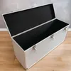 An open silver trunk with a black interior, placed on a wooden floor against a textured wall. Produktbild-Vorschau