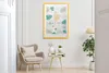 A framed picture hangs on a wall above a chair and a small side table, with a plant in a pot to the right. Náhled obrázku produktu