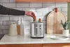 A person's hand is placing a slice of bread into a silver toaster on a kitchen counter. Anteprima dell’immagine prodotto
