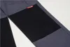 A close-up view of a pair of gray pants with a black patch on the knee and a small red tag with white text. Produktbild-Vorschau