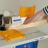A person is using a woodworking machine to cut a piece of wood. The machine has safety features and guides. Produktbild-Vorschau