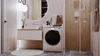 A modern bathroom with a washing machine, vanity, and shower. Produktbild-Vorschau