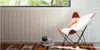 A butterfly chair with a sheepskin throw is placed on a rug in front of a fluted wall paneling, with a window showing greenery above. Náhľad obrázku produktu