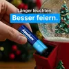 A hand inserts a battery into a Christmas-themed snow globe. Produktbild-Vorschau