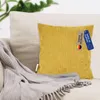 A yellow corduroy cushion with tags is placed on a sofa next to a gray knitted blanket. Produktbild-Vorschau