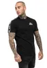 A man wearing a black t-shirt with white stripes on the sleeves and a logo on the chest. Produktbild-Vorschau