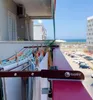 A clothes drying rack attached to a balcony railing with laundry hanging on it, overlooking a parking lot and the sea. Voir les images du produit