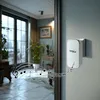A wireless doorbell receiver is mounted on a wall next to a large window overlooking a room with plants and furniture. Musical notes are depicted as emanating from the doorbell. Náhľad obrázku produktu