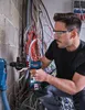 A man is using a cordless drill to drill into a wall, with many electrical wires in the background. Voir les images du produit
