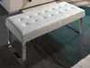 A white tufted bench with chrome legs sits on a patterned rug. Produktbild-Vorschau