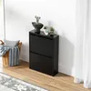 A black shoe cabinet with two flip-down doors, decorated with small potted plants on top, stands against a white wall next to a woven basket filled with pillows and blankets. Produktbild-Vorschau