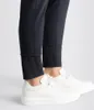 A close-up shot of a person's legs wearing black pants and white sneakers. Produktbild-Vorschau