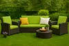 An outdoor furniture set with a sofa, two chairs, and a coffee table on a green lawn with a hedge in the background. Anteprima dell’immagine prodotto