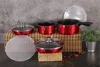 A set of red cookware is displayed on a bamboo mat with a plant and decorative petals in the background. Podgląd zdjęcia produktu