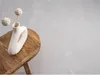A white vase with decorative spheres on sticks sits on a wooden stool against a light gray textured background. Náhled obrázku produktu