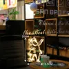 A decorative LED light in the shape of a figure is hanging in a window, with text visible on the window. Produktbild-Vorschau