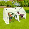 A mini greenhouse with potted plants on a grassy lawn in front of a house and garden. Produktbild-Vorschau