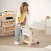 A young girl is playing with a wooden toy shopping cart in a room with a toy store setup. Produktbild-Vorschau