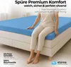 A person sitting on a bed with a blue fitted sheet. Produktbild-Vorschau