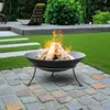 A fire pit with burning logs in a backyard setting with artificial grass and stone paving. Produktbild-Vorschau