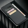 A close-up shot of a black leather iPhone case with card slots and a banknote. The case is placed on a dark, textured surface. Voir les images du produit