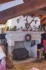 A rustic living room scene featuring a large stone fireplace adorned with various decorative items, including antlers, taxidermy birds, and a wreath. Produktbild-Vorschau