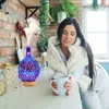 A woman is sitting at a kitchen counter, holding a mug and looking at an aroma diffuser. Voir les images du produit