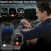 A man is looking at his smartwatch while holding his phone. The background shows a rocky coastline with the ocean. Produktbild-Vorschau