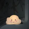 A cute cloud-shaped night light with a smiling face sits on a shelf in a dimly lit room. Voir les images du produit
