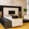 A modern living room with a large wall clock, television, speakers, and a sectional sofa. Produktbild-Vorschau