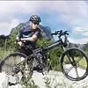 A man in cycling gear poses with an electric bicycle in a mountainous, outdoor setting. Produktbild-Vorschau