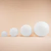 Four white spheres of increasing size are arranged in a line on a light peach background. Produktbild-Vorschau