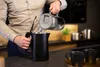 A person is pouring water from a glass pitcher into a black electric kettle in a modern kitchen. Produktbild-Vorschau