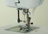 A close-up view of the needle and presser foot area of a sewing machine, with red thread being guided through the mechanism. Produktbild-Vorschau
