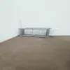 A metal cage trap is placed on a brown surface against a white wall. Voir les images du produit